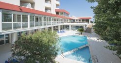 Complesso alberghiero con piscina circondata da edifici moderni e alberi.