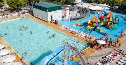 Vista aerea di una piscina con scivoli e area giochi colorata, circondata da lettini.
