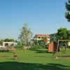 Un parco giochi con altalene, prato verde, e case in lontananza.