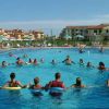 Gruppo di persone in cerchio in una grande piscina, con edifici residenziali sullo sfondo.