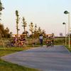 Persone su veicoli a pedali percorrono un sentiero circondato da alberi in un parco.