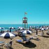 Spiaggia con file di ombrelloni blu e bianchi, sdraio e una torretta di salvataggio vicino al mare.