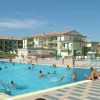 Una piscina all'aperto con persone che nuotano, circondata da edifici a due piani e ombrelloni.