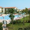 Vista di una piscina con lettini, ombrelloni, edifici circostanti e un giardino alberato.