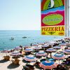 Spiaggia con ombrelloni colorati e insegna di una pizzeria.