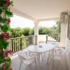 Terrazzo con tavolo bianco e sedie, vista su vegetazione verde.
