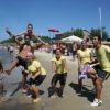Un gruppo di persone in magliette gialle che sorride e fa pose divertenti su una spiaggia.