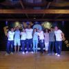 Un gruppo di persone in posa su un palco di legno con una scritta colorata sullo sfondo.