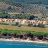 Complesso residenziale vicino a una spiaggia con pini e colline sullo sfondo.