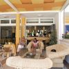 Due persone sedute in un'area lounge con divani intrecciati e soffitto a strisce arancioni.