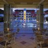 Terrazza con tavoli e sedie, vista serale su piscina e edificio illuminato.