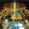 Vista notturna di un hotel con piscina illuminata e ospiti attorno a tavoli e ombrelloni.