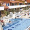 Piscina all'aperto con ospiti che nuotano, lettini e ombrelloni, di fronte a edifici colorati.