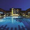 Piscina illuminata di sera davanti a un grande edificio con balconi.