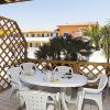 Tavolo rotondo bianco con sedie su un patio, palme e edifici sullo sfondo.