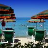 Ombrelloni verdi e arancioni su una spiaggia, persone che nuotano in mare.