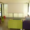Sala con sedie colorate, grande schermo bianco e finestre luminose.