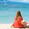 Famiglia in spiaggia seduta sulla sabbia, di fronte al mare azzurro.