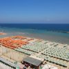 Spiaggia con ombrelloni arancioni e verdi disposti in file ordinate, mare azzurro sullo sfondo.