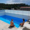 Due persone sedute sul bordo di una piscina su una terrazza con vista su colline e edifici.
