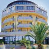 Facciata di hotel giallo con palme e balconi.