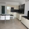 Cucina moderna con mobili chiari, tavolo nero con sedie bianche e TV su mobile.