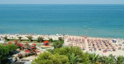 Spiaggia con ombrelloni e lettini, vista mare e vegetazione verde.