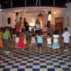 Bambini e adulti in cerchio su pavimento a scacchi.
