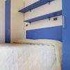 Letto con copriletto bianco, scaffali blu a muro, armadio blu e pavimento in legno chiaro.