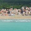 Vista aerea di una spiaggia con edifici residenziali e una foresta sullo sfondo.