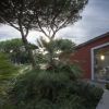 Un edificio rosso con ampia finestra accanto a palme e alberi sotto un cielo nuvoloso.