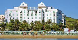 Grande edificio bianco sul lungomare, palme in primo piano.
