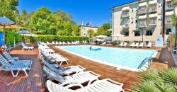 Piscina all'aperto con lettini bianchi su una terrazza in legno, circondata da alberi.