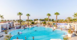 Grande piscina con palme e persone che nuotano, circondata da lettini.