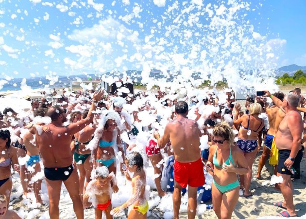 Festa in spiaggia con schiuma e molte persone.