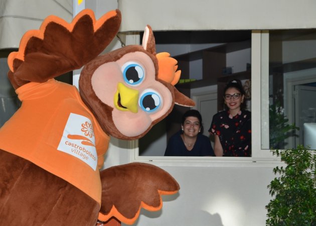 Mascotte di gufo marrone con due persone sorridenti alla finestra.