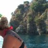 Due persone in barca guardano verso scogliere e mare.