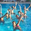 Gruppo di persone in acqua alzano le braccia in piscina.