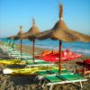 Spiaggia con ombrelloni di paglia e lettini verdi.