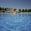 Vista di una piscina con uno scivolo blu e giallo sullo sfondo. Uomo su galleggiante.