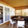 Veranda con tavolo in legno, sedie bianche e divani marroni. Interno di una cucina visibile.