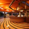Hall con reception circolare, pavimento a strisce ondulate e soffitto in legno con luci calde.