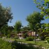 Giardini verdi con bungalow in legno sullo sfondo tra alberi e cespugli sotto un cielo blu.