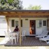 Esterno di una casa mobile con terrazza, tavolo e sedie da giardino sotto una tettoia.