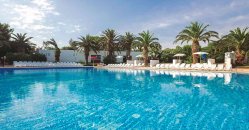 Piscina con lettini bianchi e palme intorno sotto un cielo parzialmente nuvoloso.