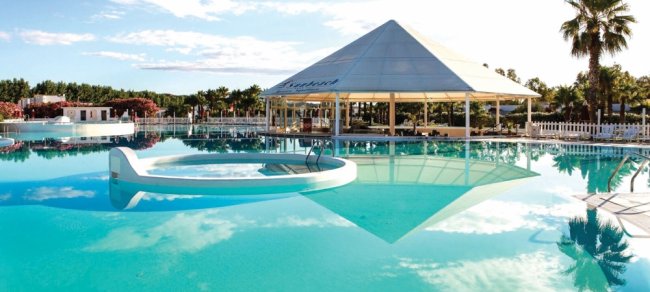 Piscina con gazebo al centro e cielo riflesso sull'acqua.