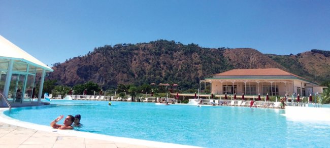 Piscina con sfondo montuoso e persone che nuotano.