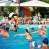 Persone che giocano in piscina, lettini e ombrelloni sullo sfondo.