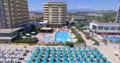 Piscina circondata da lettini e ombrelloni, con un grande edificio sullo sfondo.