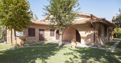 Una casa di mattoni con tetto in tegole, circondata da alberi e prato.
